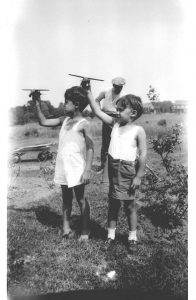 Bill and Howard "flying" model airplanes while Dad raked the yard.